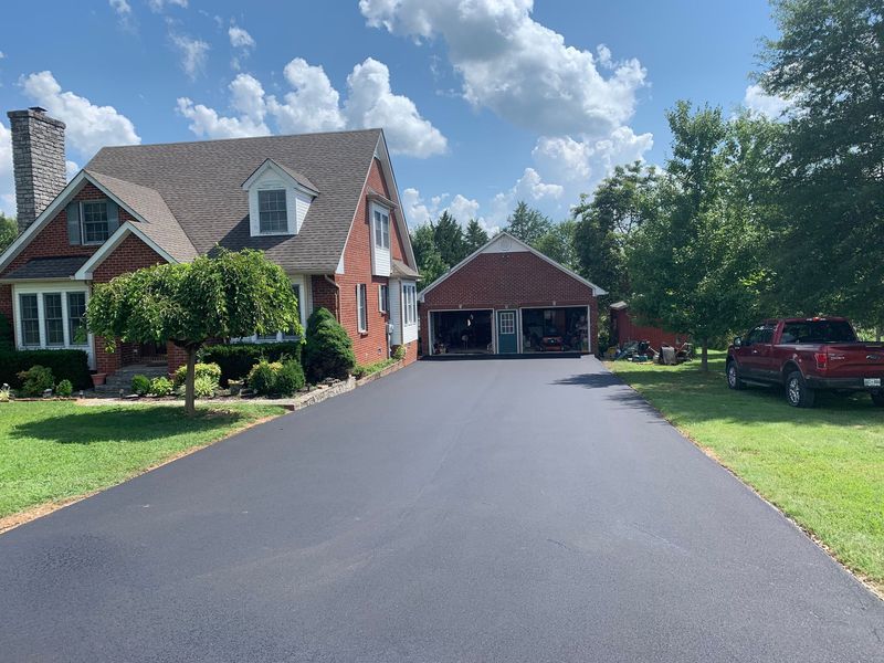 A red brick house with a long, dark asphalt driveway and a detached garage.