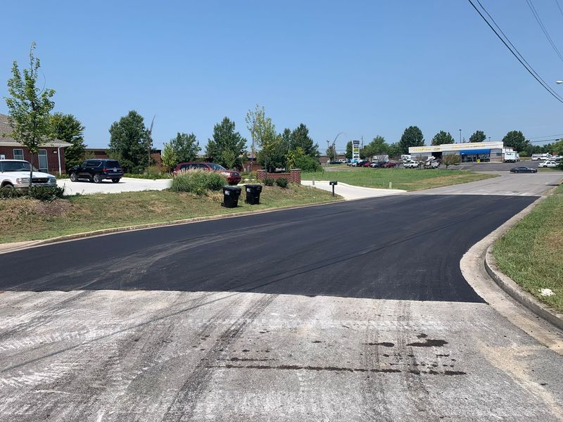 Newly paved road with black asphalt meets older road. Clear sky.