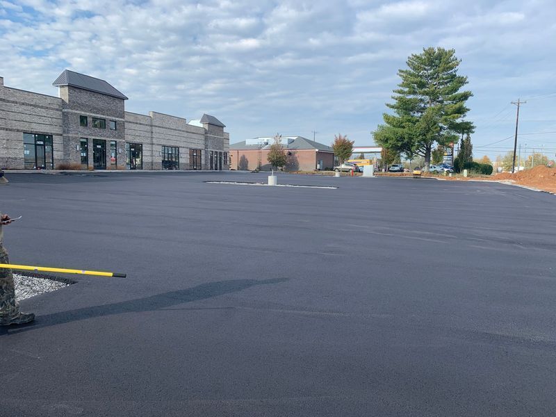 Newly paved, empty parking lot in front of a commercial building under a cloudy sky.