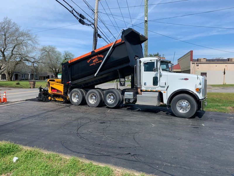 A white dump truck unloading asphalt into a paving machine on a road.