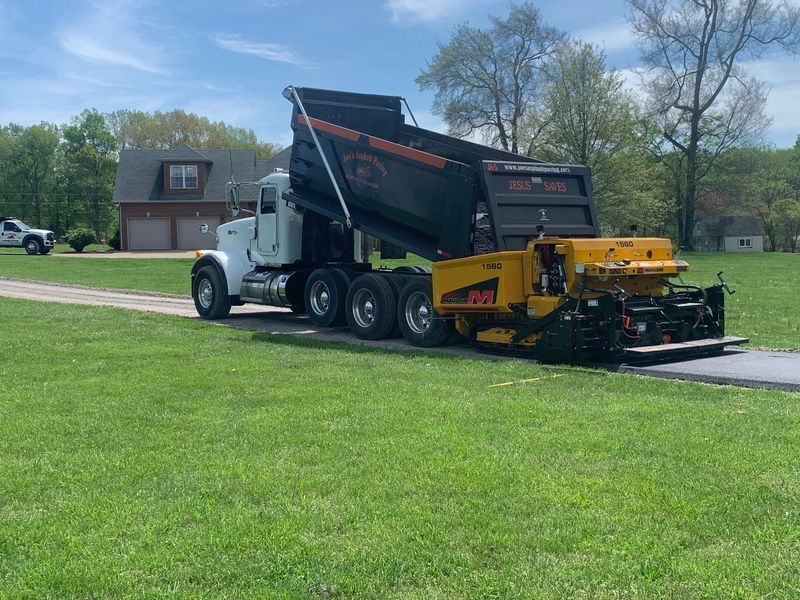 A dump truck unloading asphalt into a paving machine on a driveway.