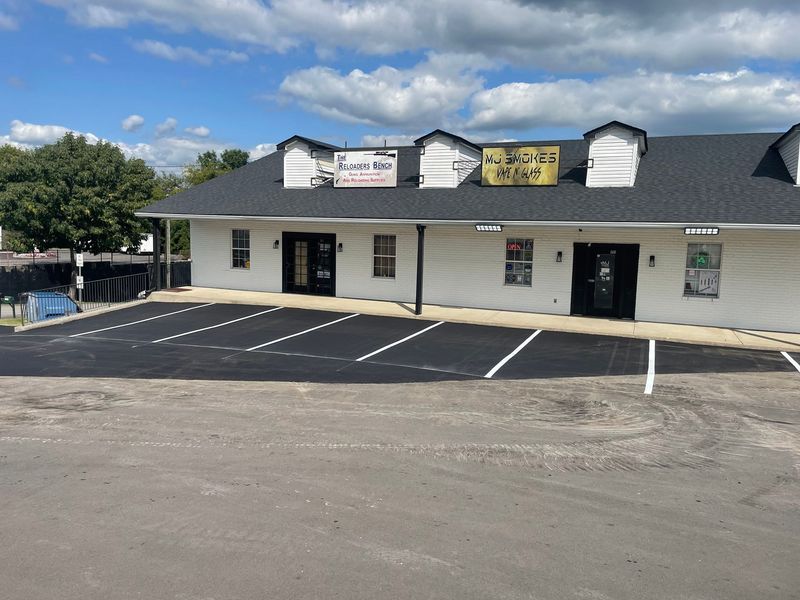 A white one-story commercial building with black trim, parking lot in front, and signs on the roof.