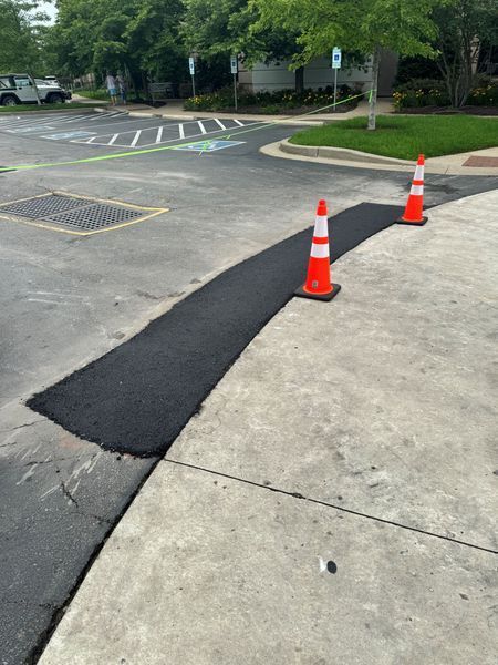 Asphalt repair with two orange traffic cones on a concrete curb. Parking lot setting.