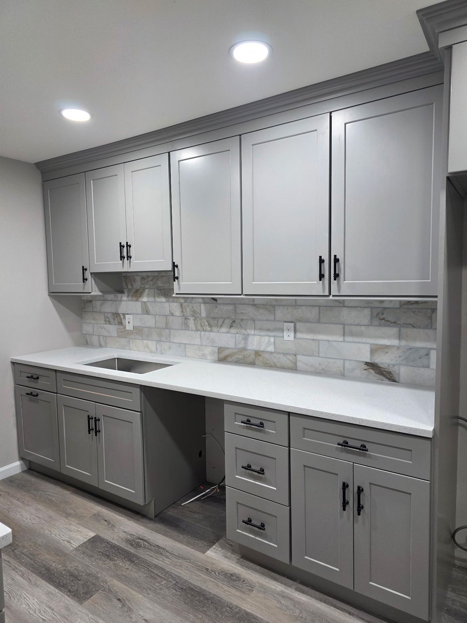 Gray kitchen cabinets with white countertop and textured backsplash.