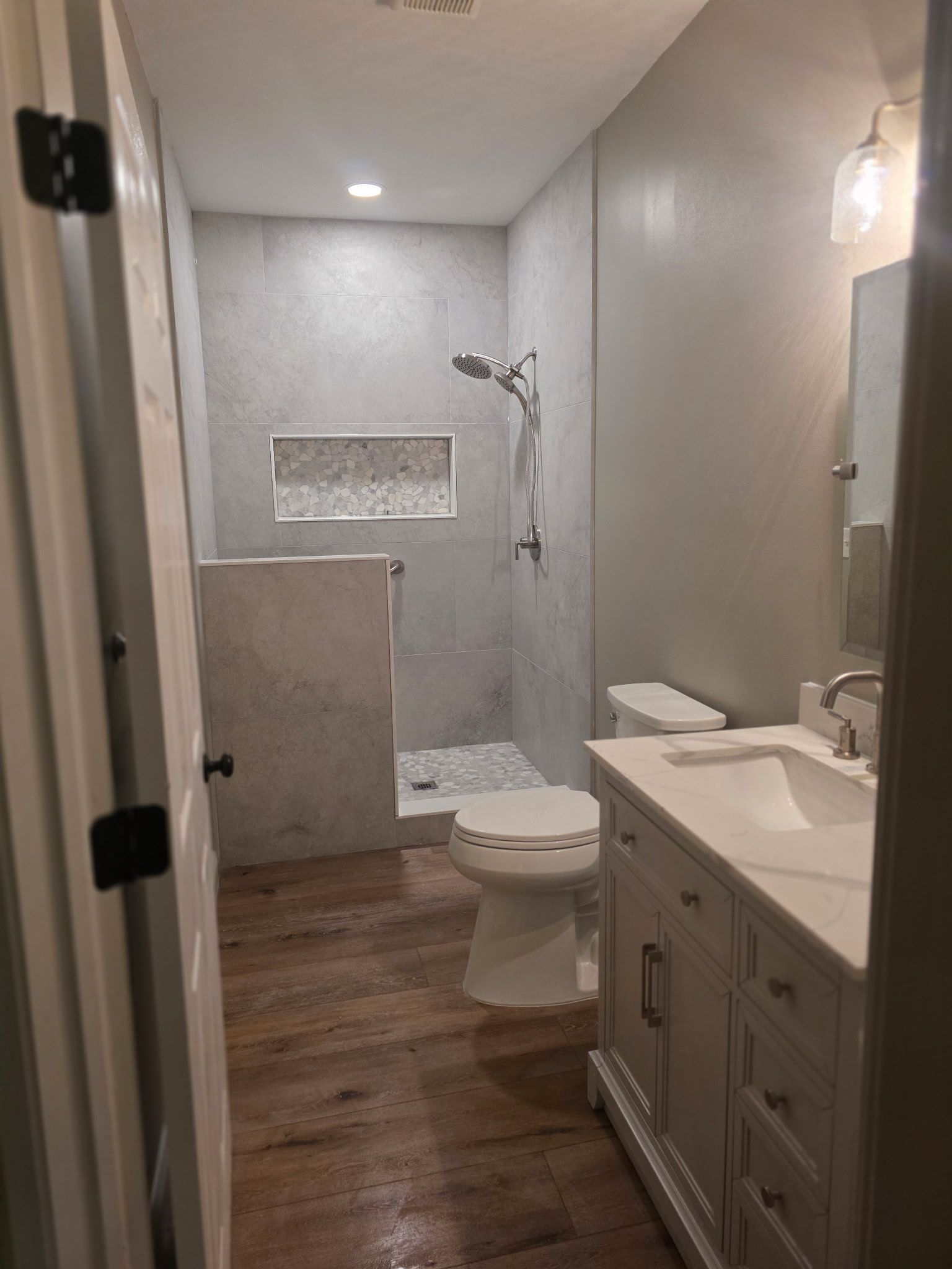 Bathroom with gray tiled shower, white vanity, and wooden floor.