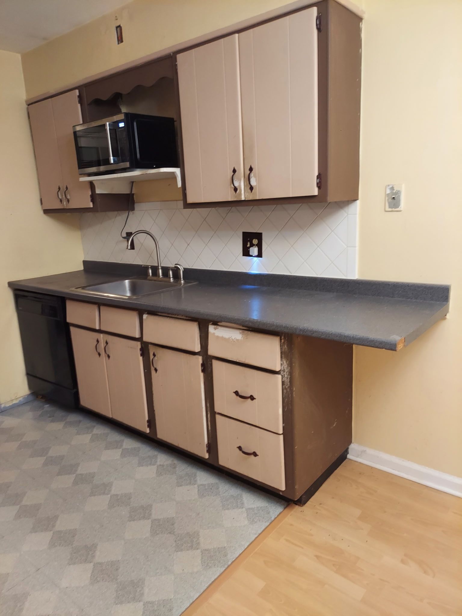 Kitchen with beige cabinets, microwave, dark countertops, and linoleum flooring.