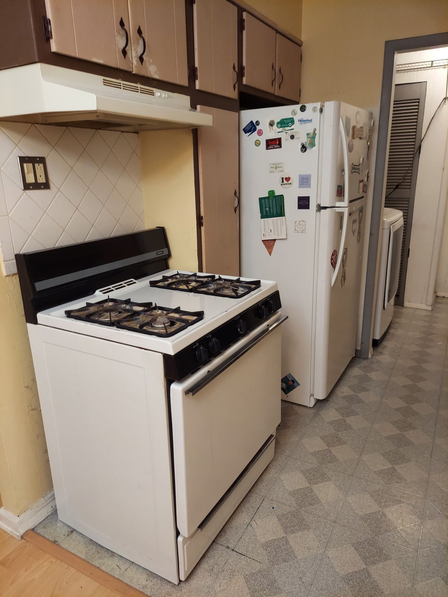 White kitchen stove and refrigerator in a small kitchen. Cabinets and appliances line the wall.