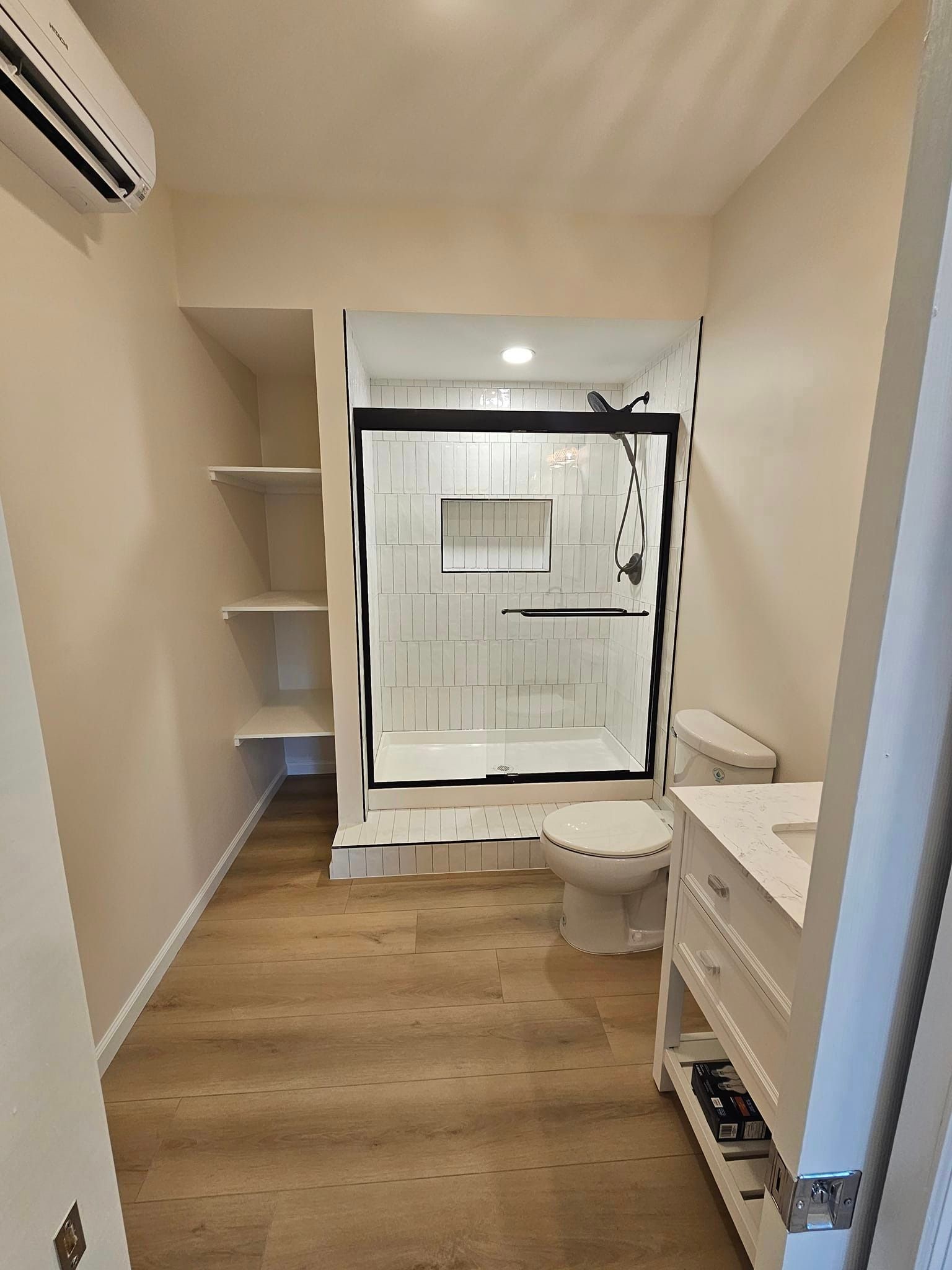 A bathroom with a toilet, sink, shower and air conditioner.