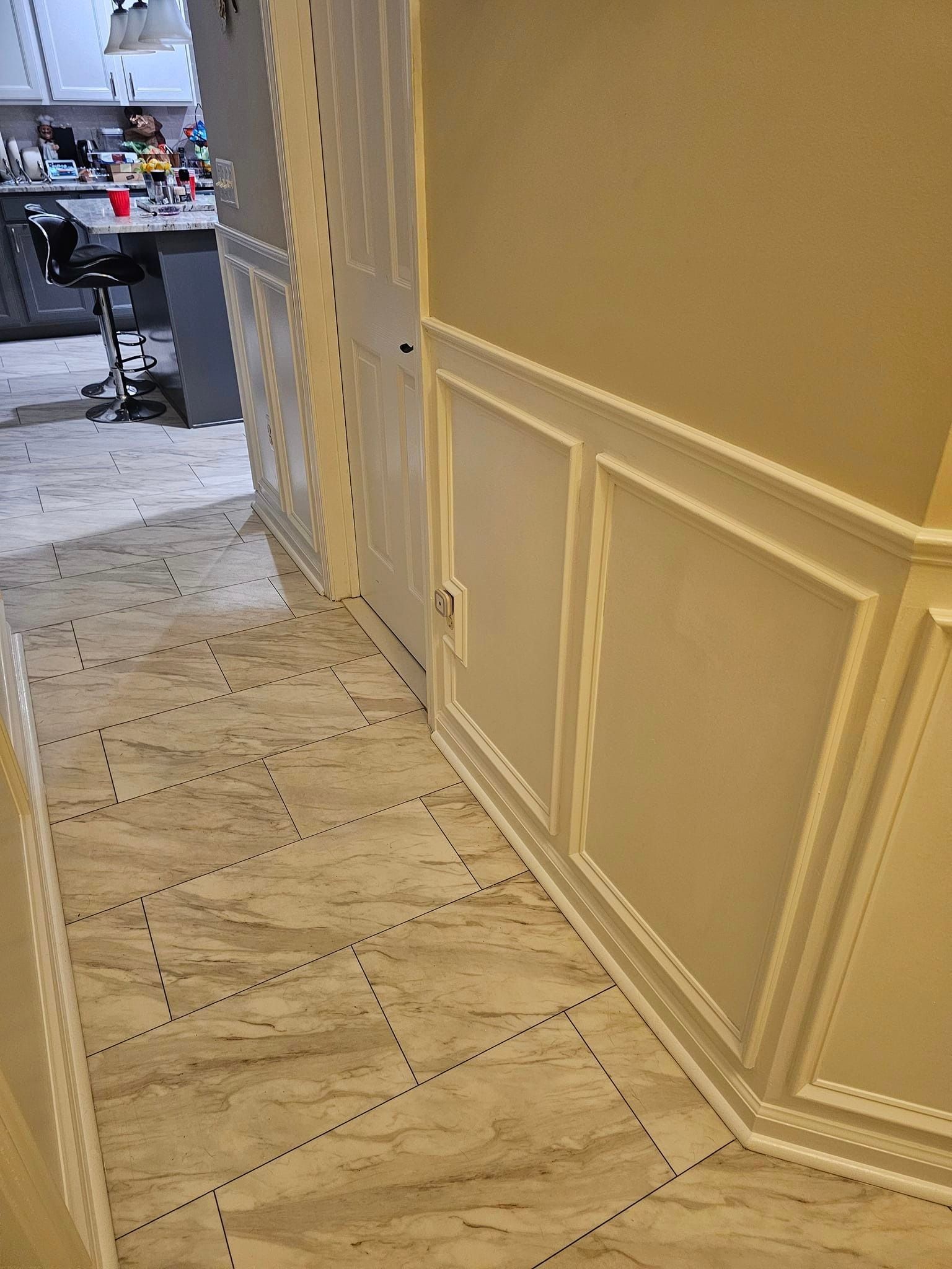 A hallway with tile floors and white trim leading to a kitchen.