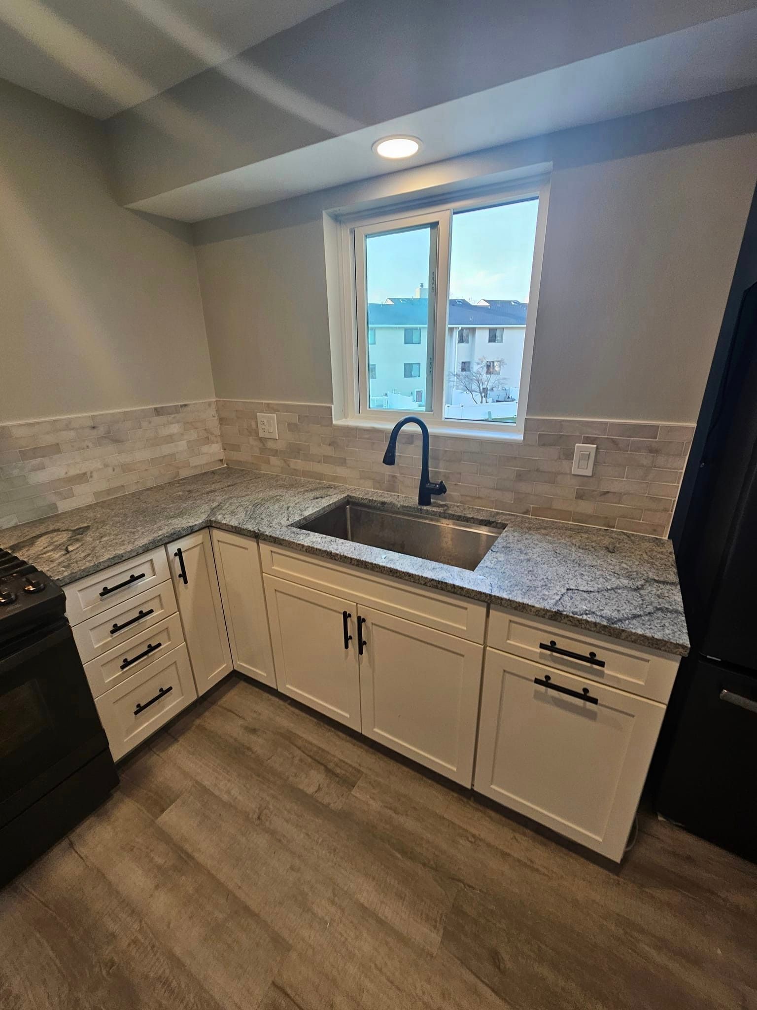 A kitchen with white cabinets, granite counter tops, a sink and a window.