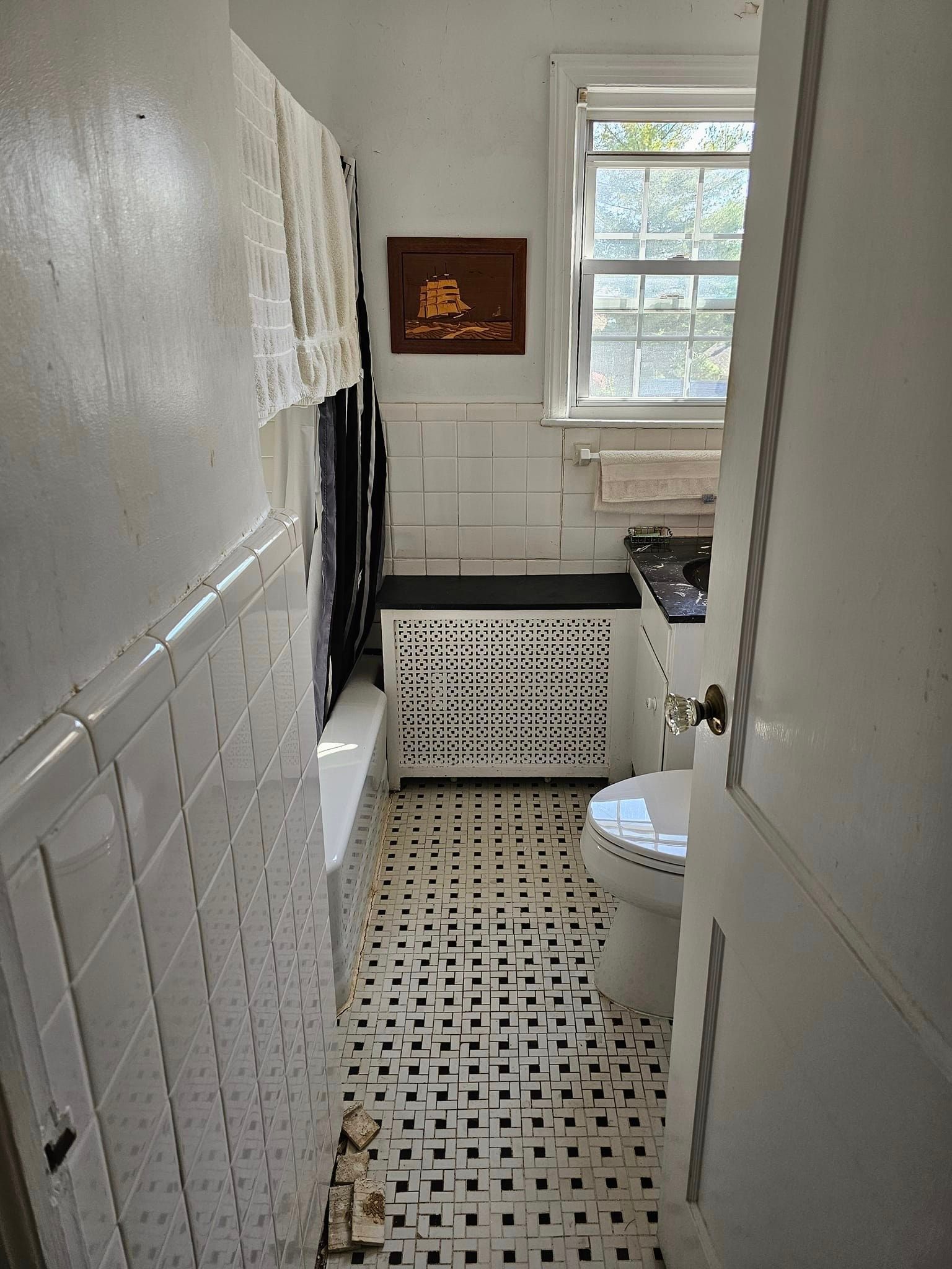 A bathroom with white tiles, a toilet, and a window.