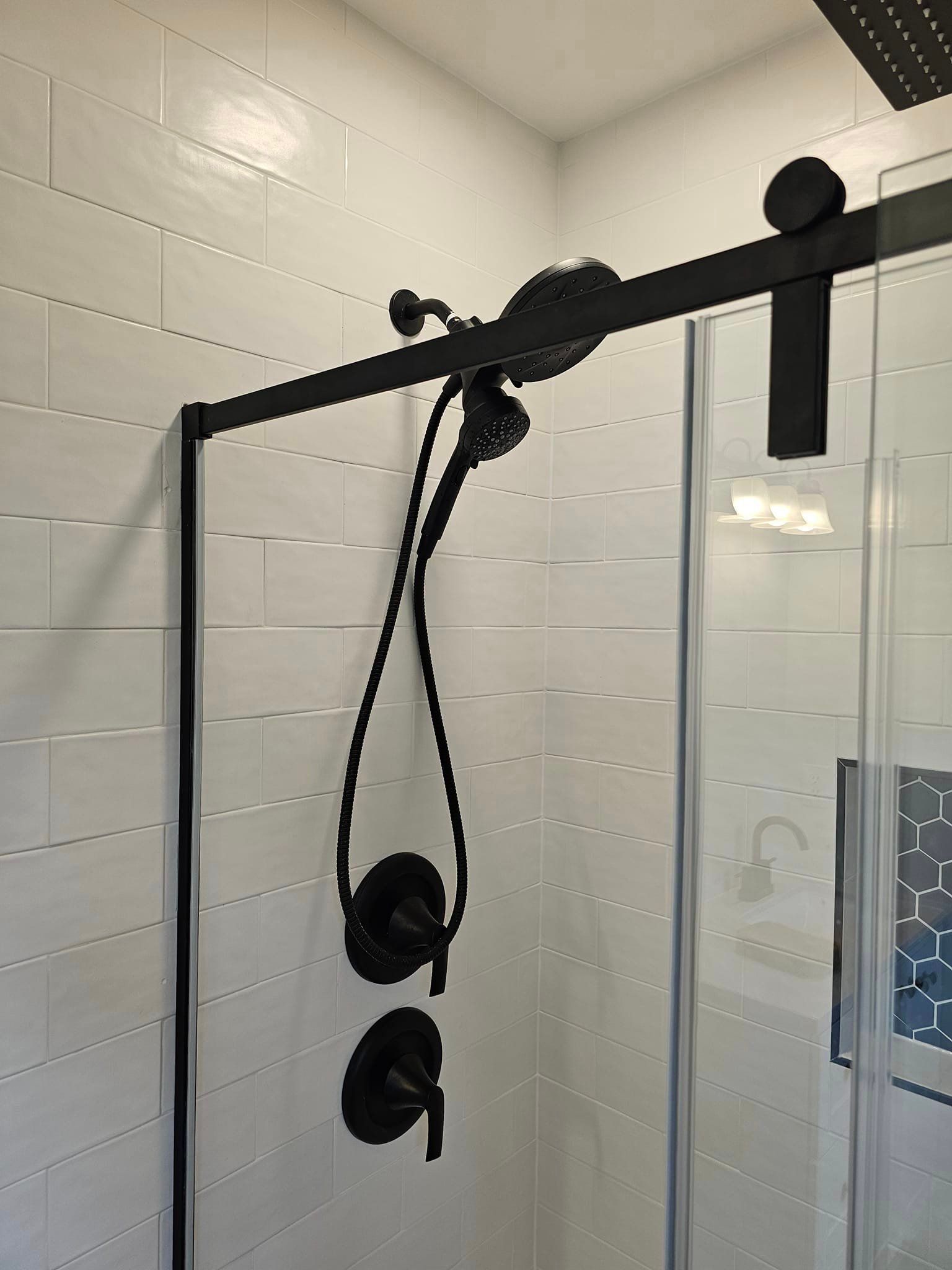 A black shower head is hanging from a sliding glass door in a bathroom.