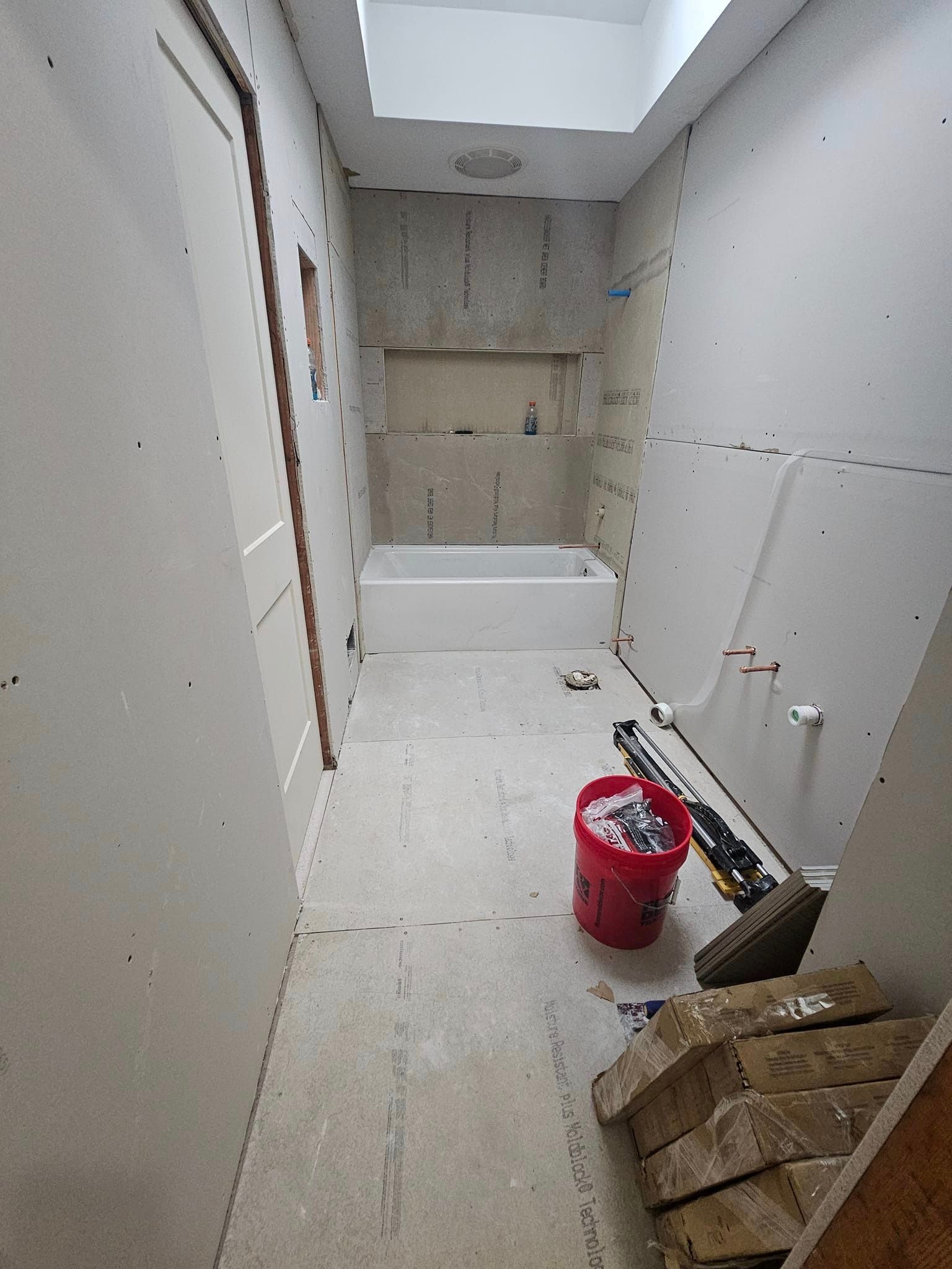 A bathroom under construction with a bathtub and a red bucket on the floor.