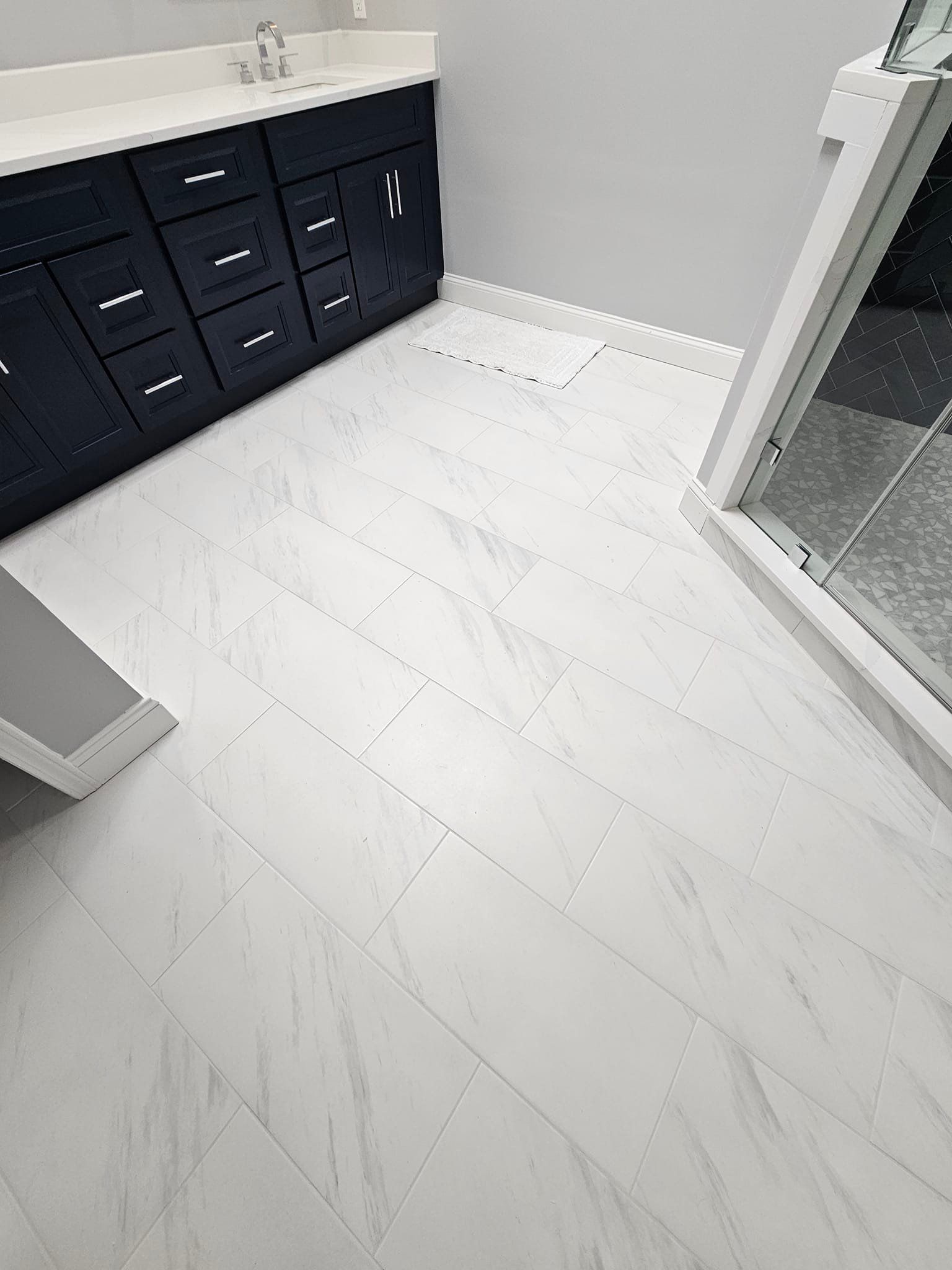 A bathroom with white tile floors and black cabinets.