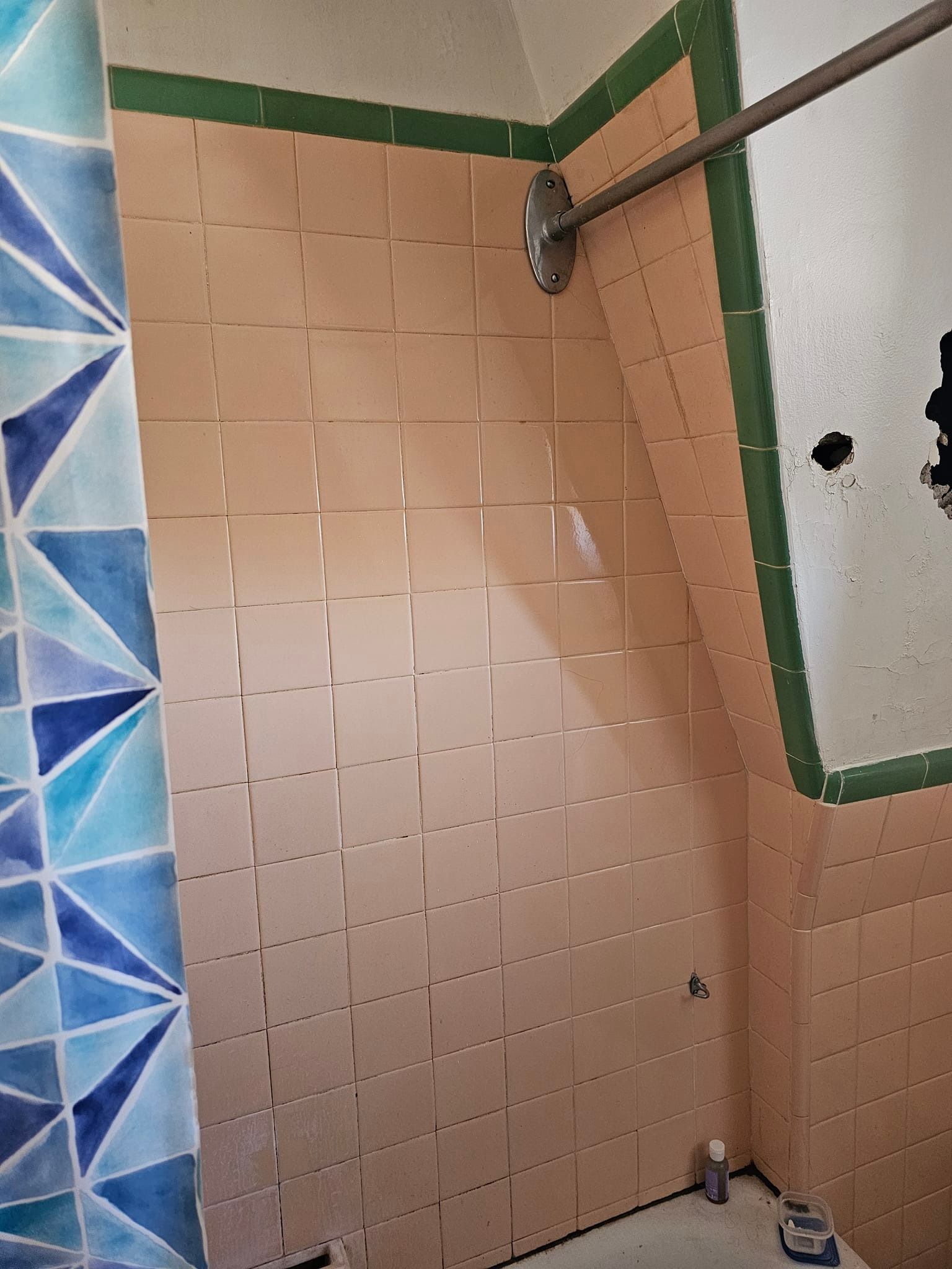 A bathroom with pink and blue tiles and a shower head.