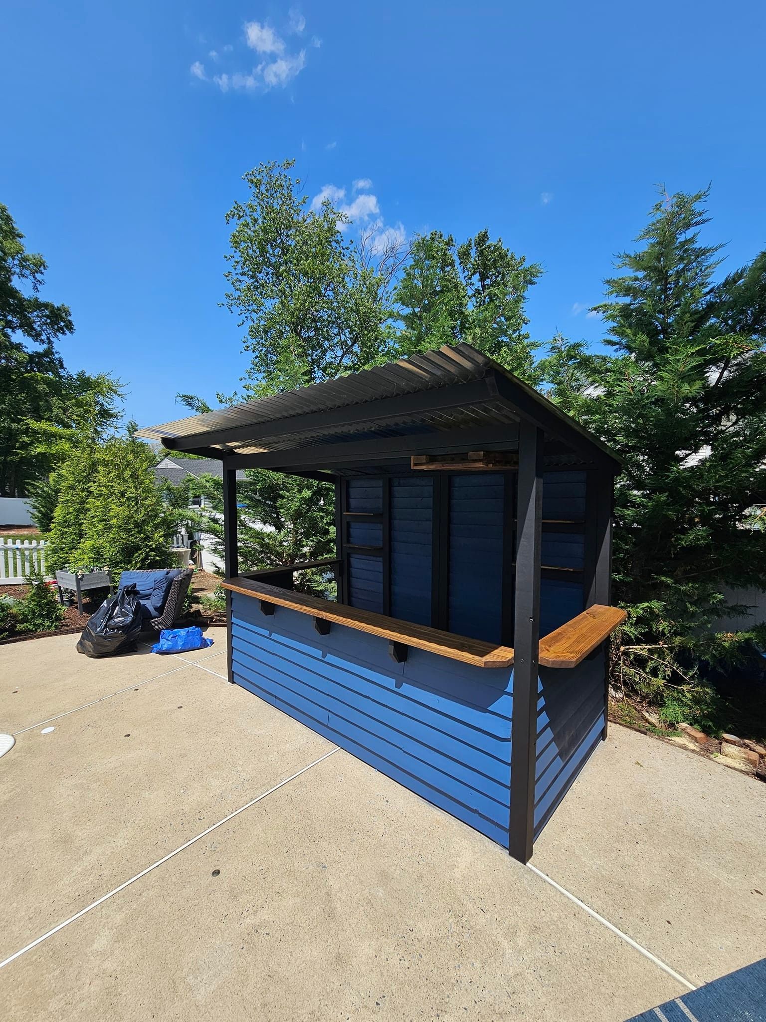 A blue wooden shack with a wooden bar is sitting in a parking lot.