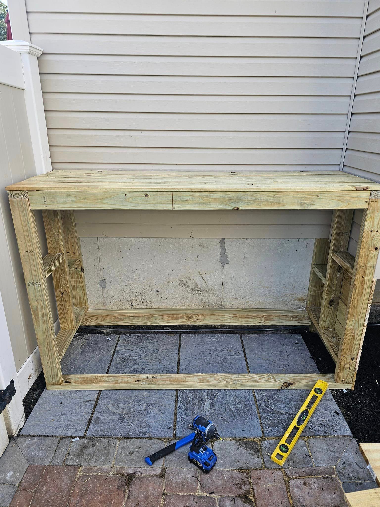 A wooden bench is sitting on a brick patio next to a wall.