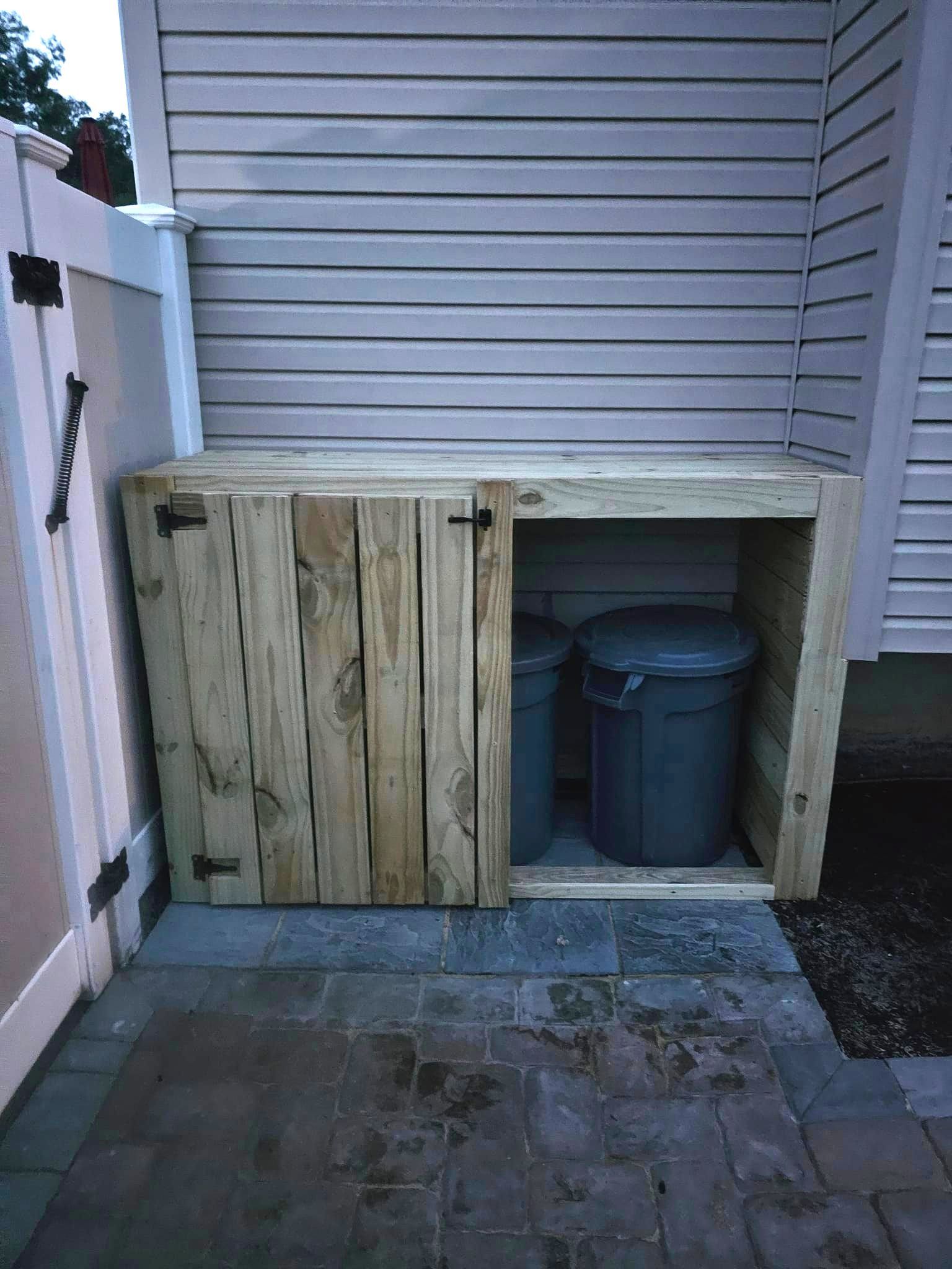 A wooden trash can shed with two trash cans inside of it.