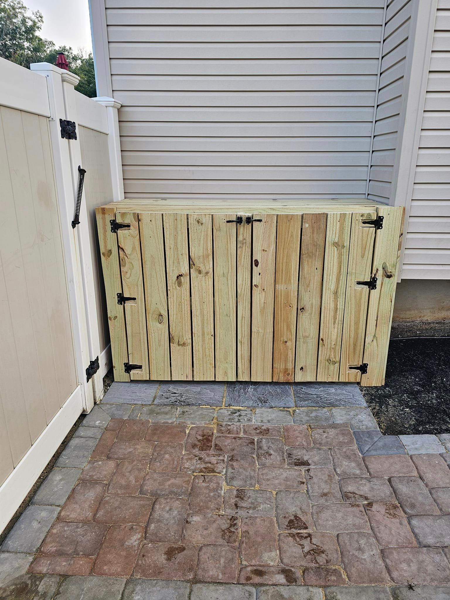 A wooden box is sitting on a brick sidewalk next to a white fence.