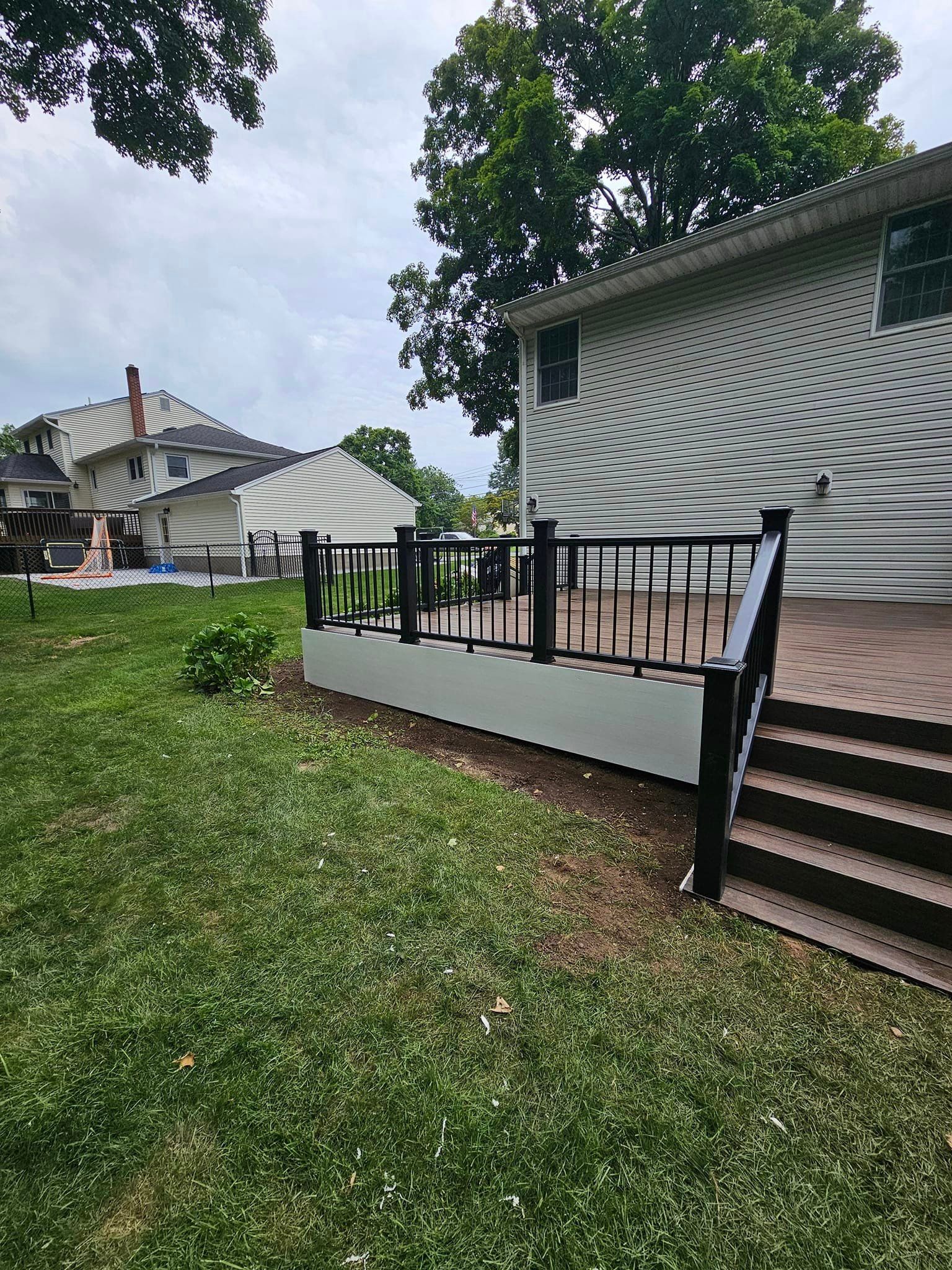 A large deck with stairs leading up to it is in the backyard of a house.