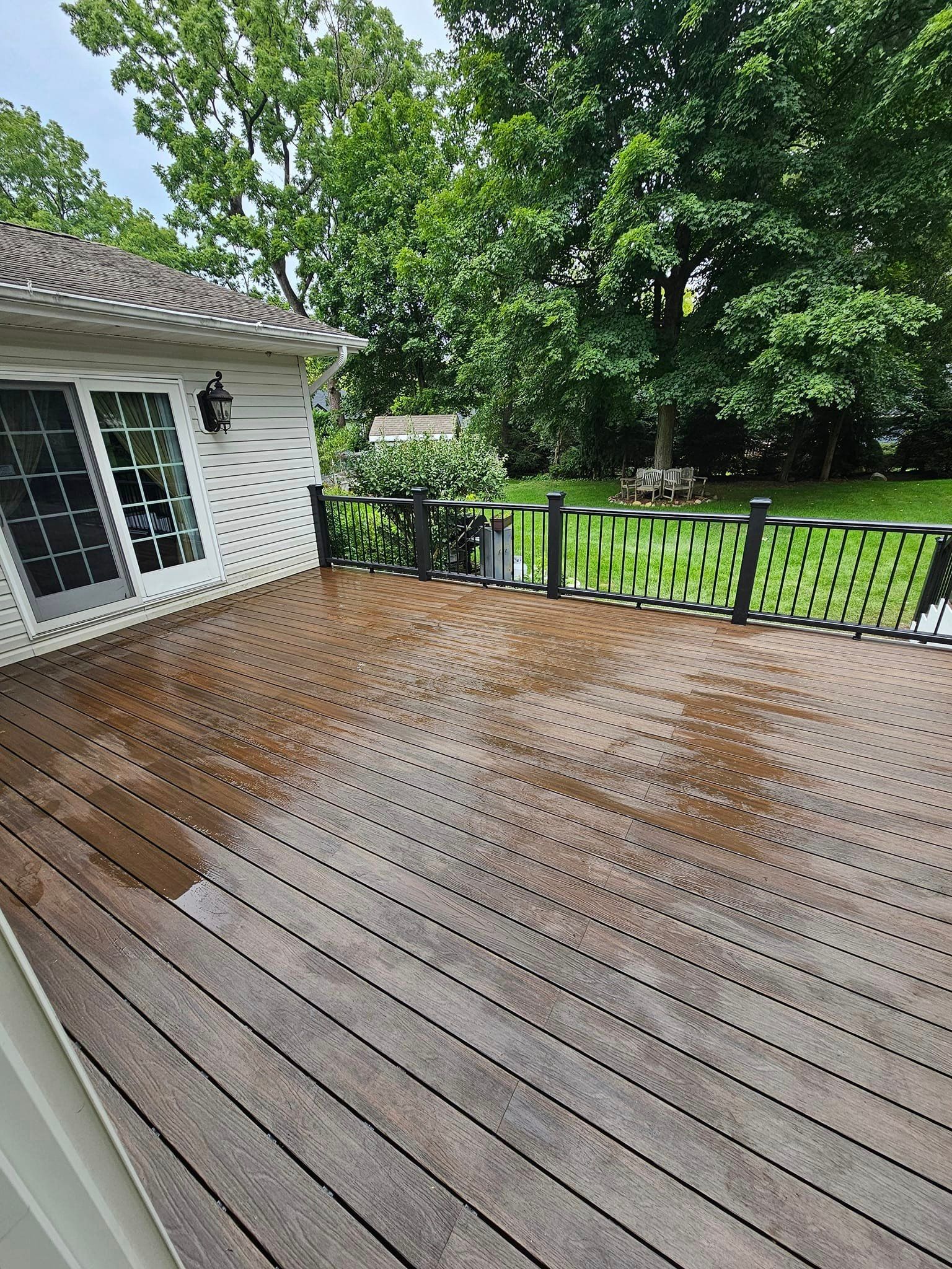 A wooden deck with a railing and a white house in the background.