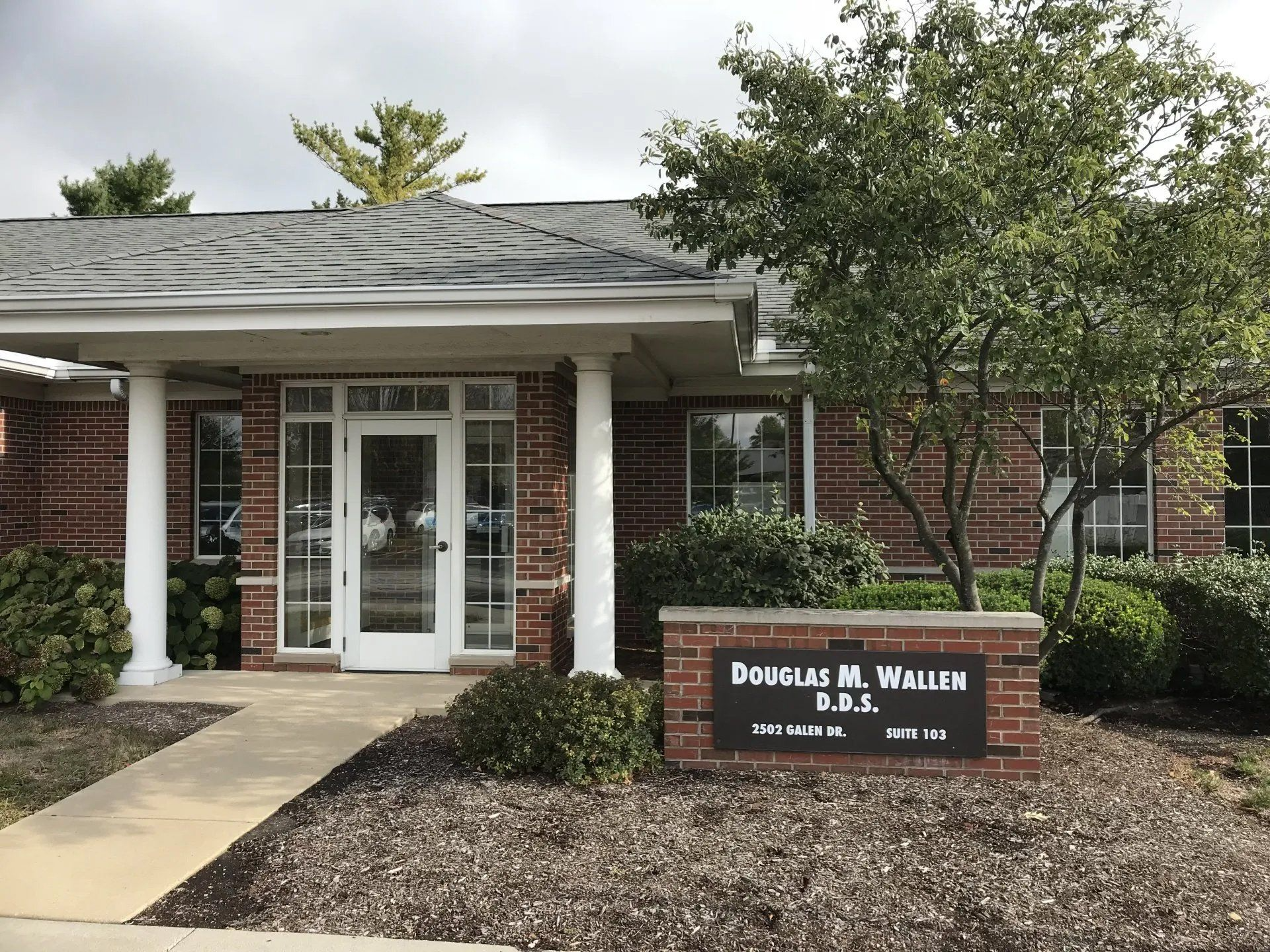 Exterior of Douglas M. Wallen, D.D.S. dental office. Brick building, sign, trees, and blue sky.