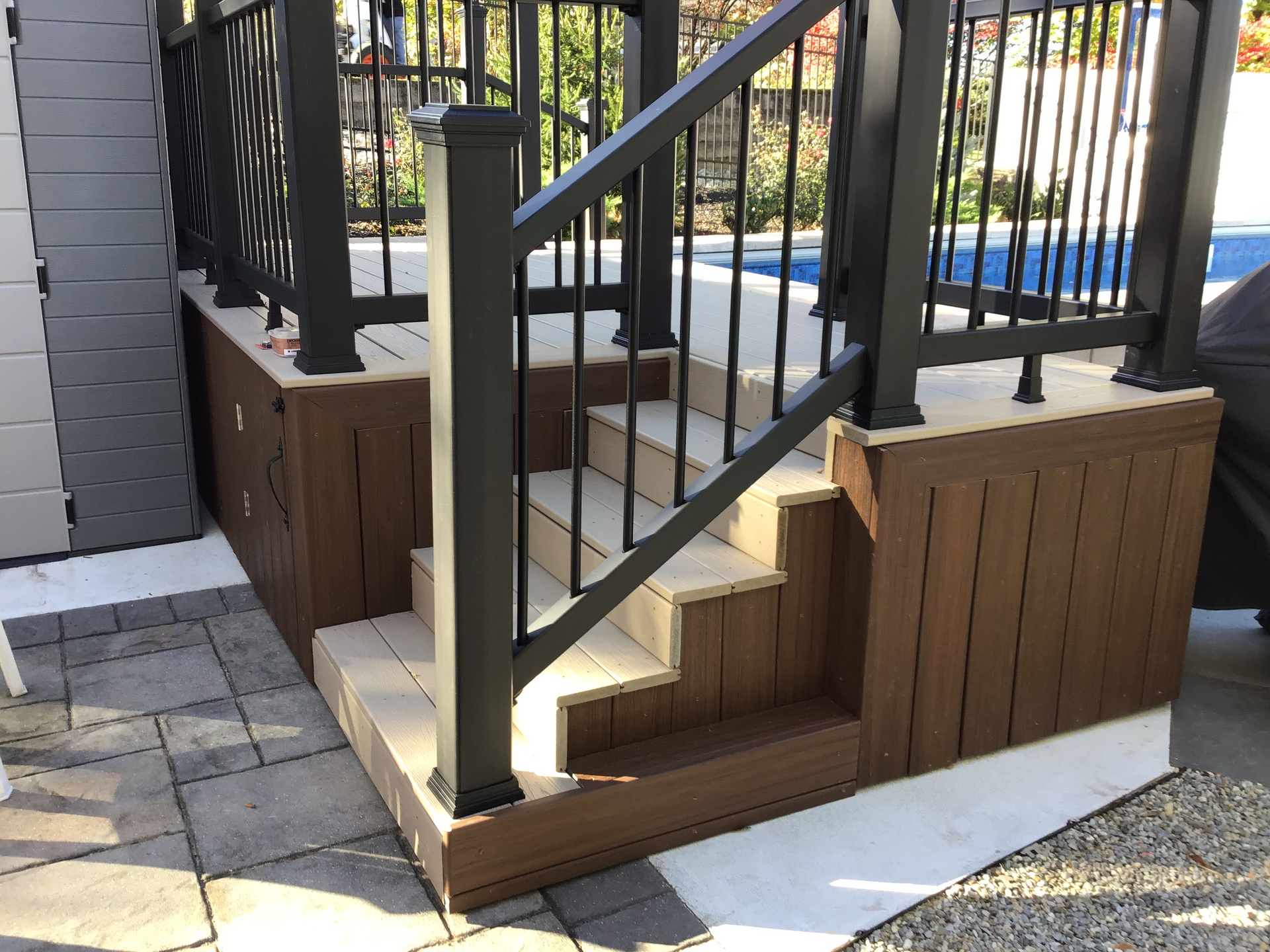 Wooden deck steps leading to a deck with black railing near a pool.