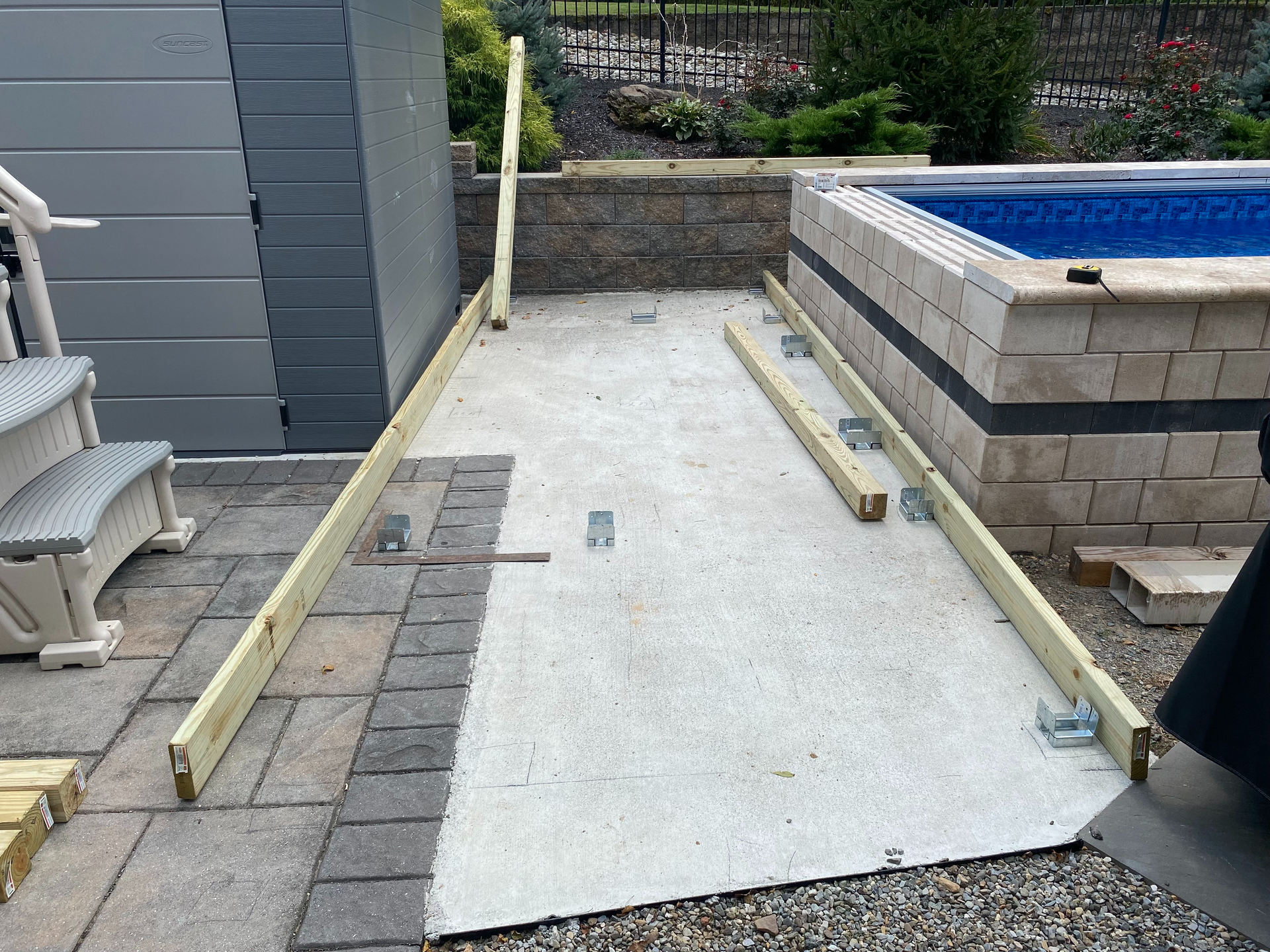 Construction of wooden frames on a concrete surface next to a pool and shed.