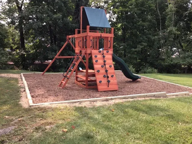 A playground with a slide, a climbing wall, and mulching ground