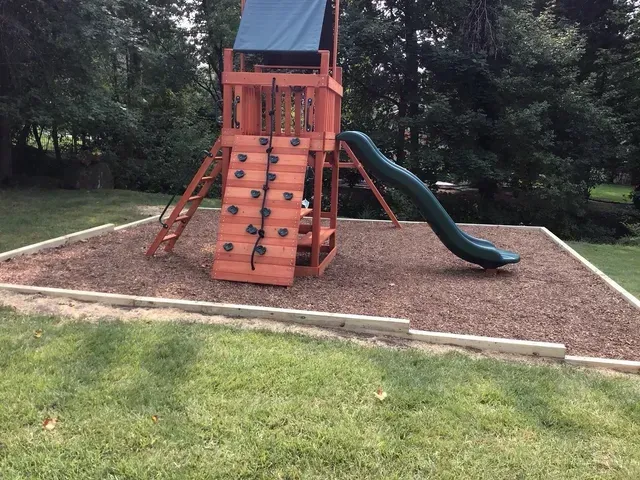 A playground with a slide, a climbing wall, and mulching ground