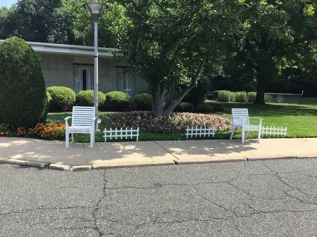 Two white chairs are sitting on the sidewalk in front of a house.