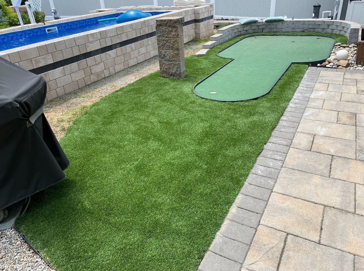 Backyard with artificial turf putting green near a pool and patio.