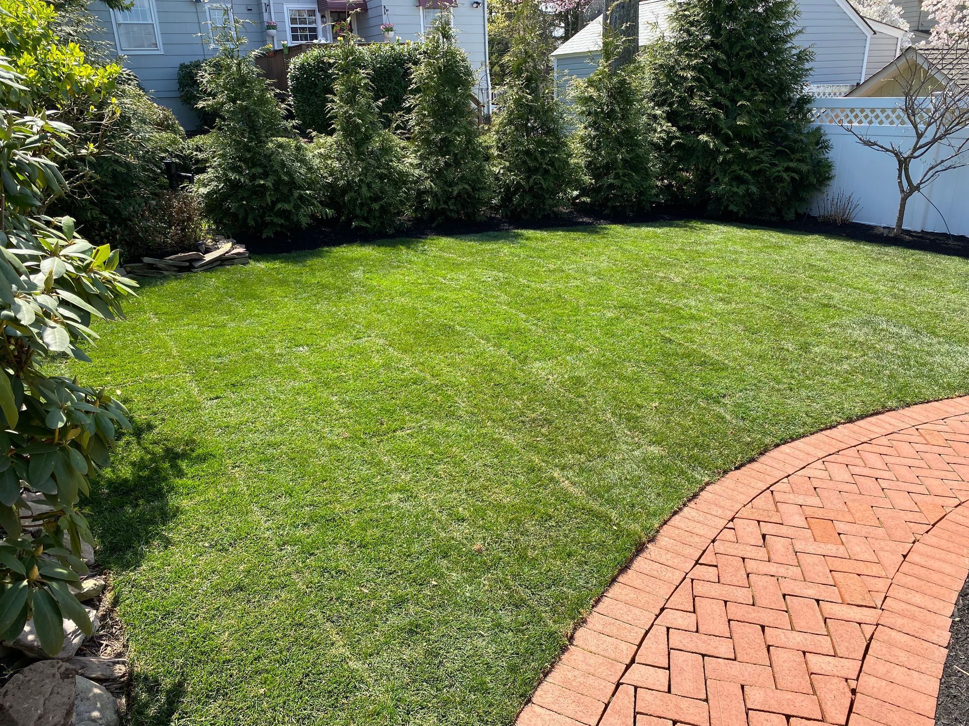 A brick walkway leading to a lush green lawn in a backyard.