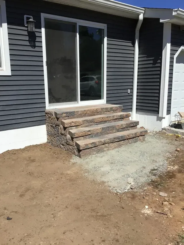 A house with stairs leading up to the front door and a sliding glass door.
