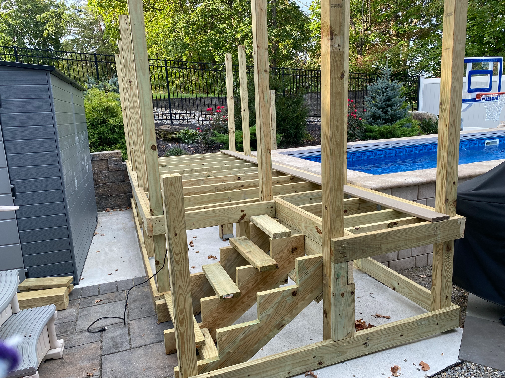 Wooden deck under construction with stairs leading to a pool area.