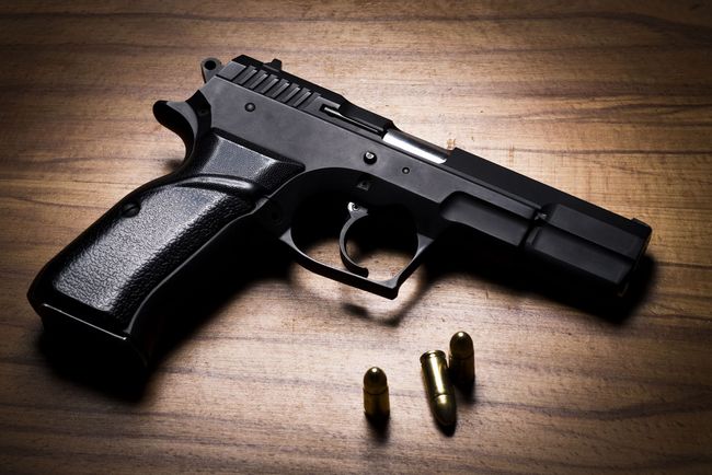 Black handgun and three bullets on a wooden surface.
