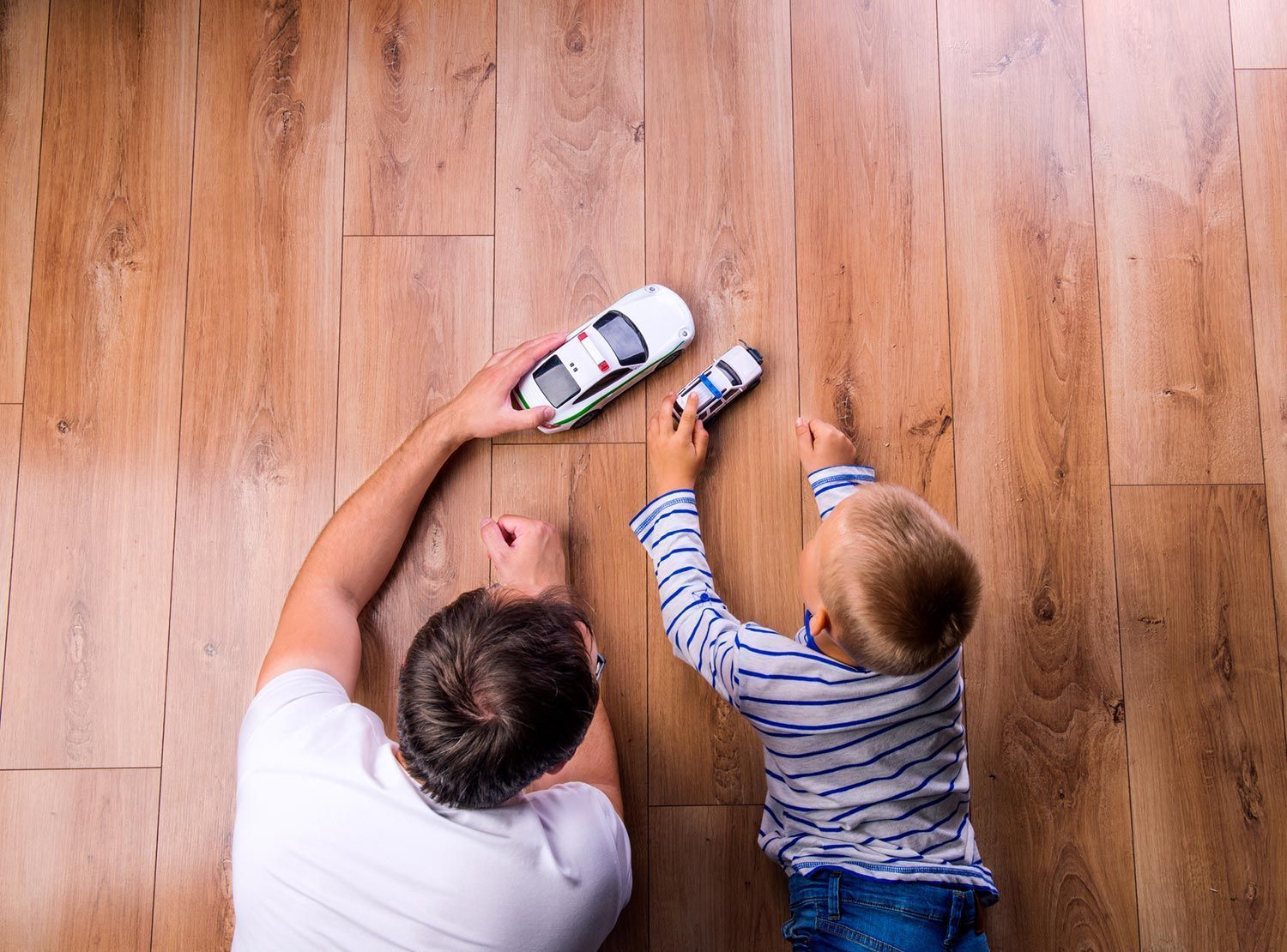A man and a child are playing with a toy car on the floor.