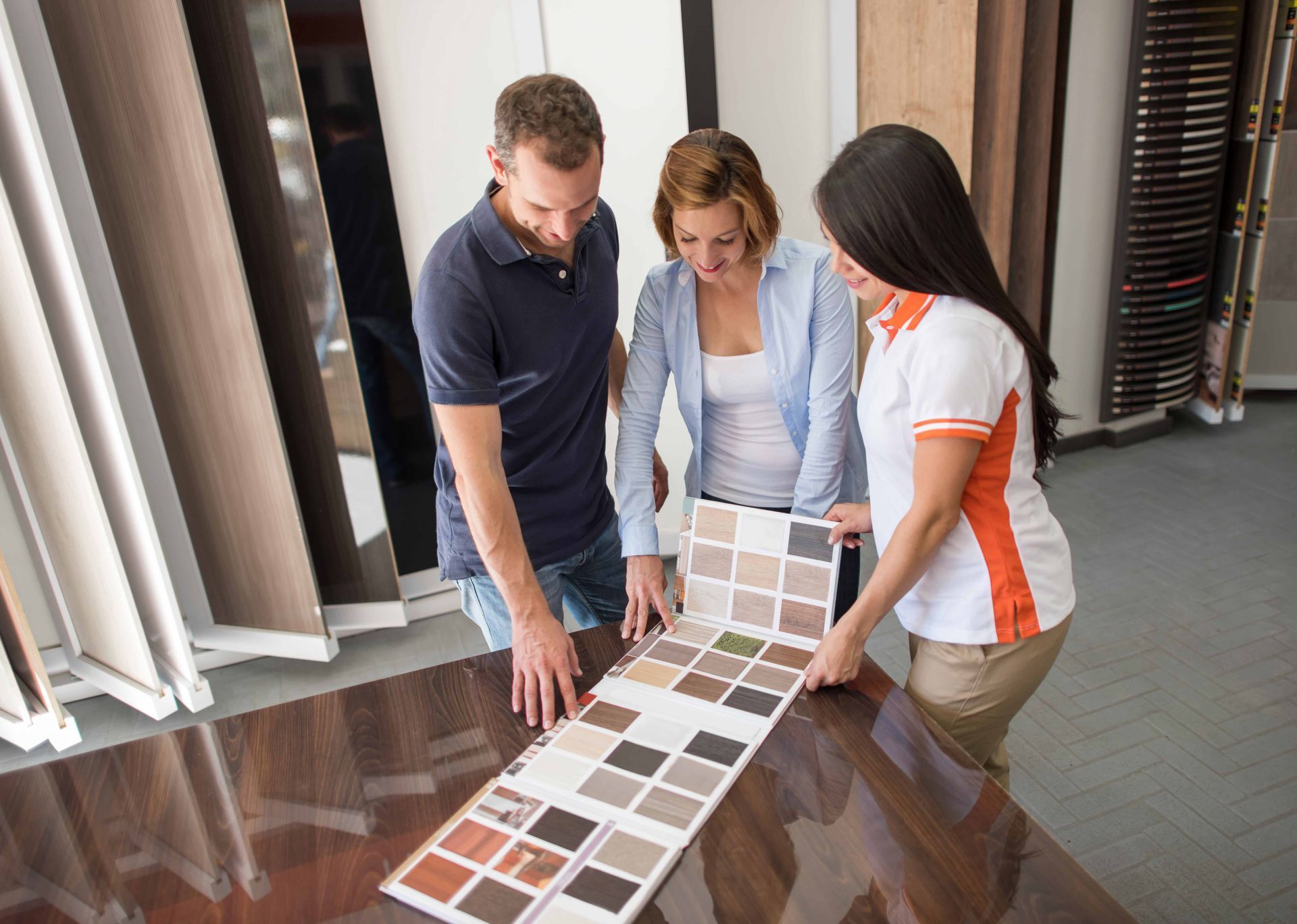 A man and two women are looking at samples of wood in a store.