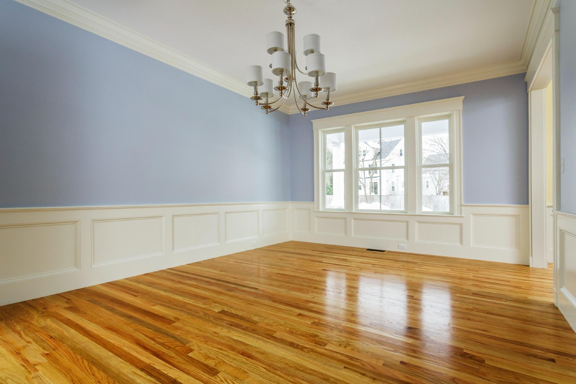 An empty room with hardwood floors , blue walls and a chandelier.