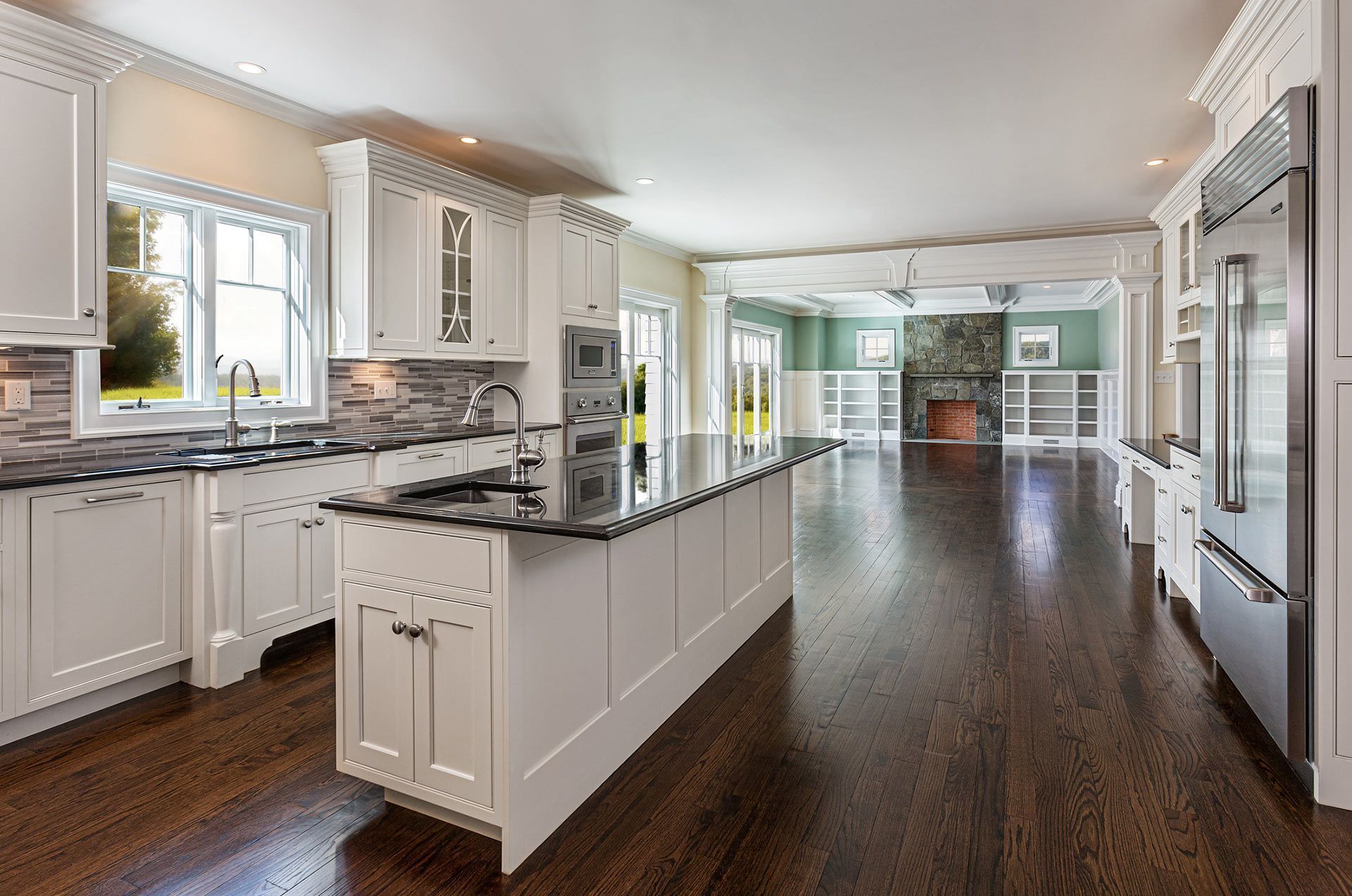 A kitchen with white cabinets , granite counter tops , stainless steel appliances and hardwood floors.