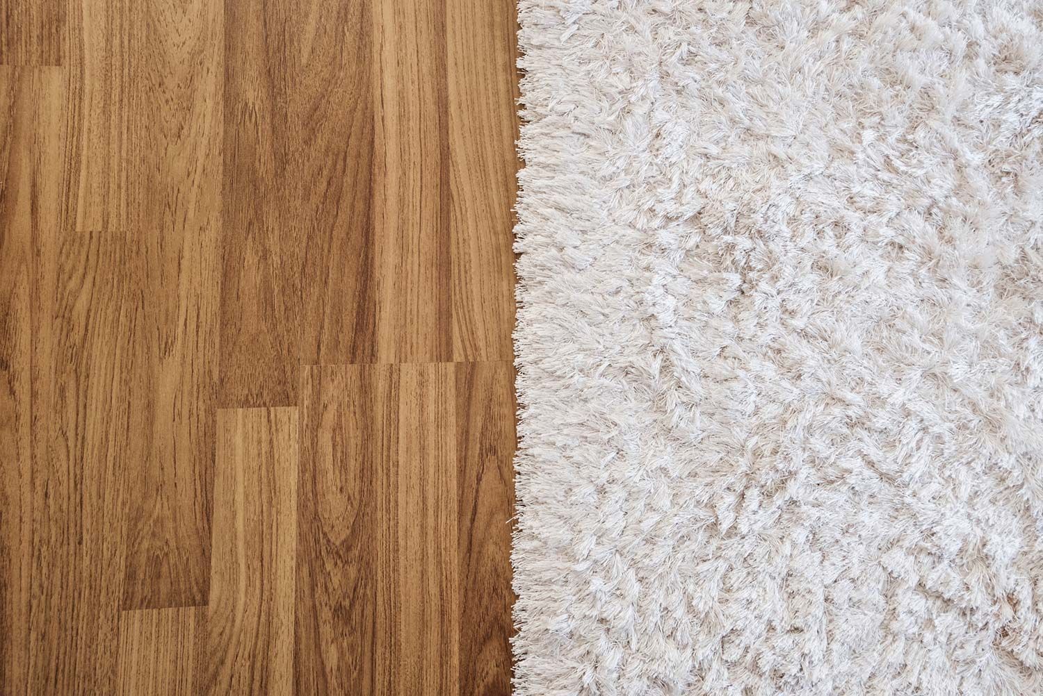 A wooden floor next to a white carpet.
