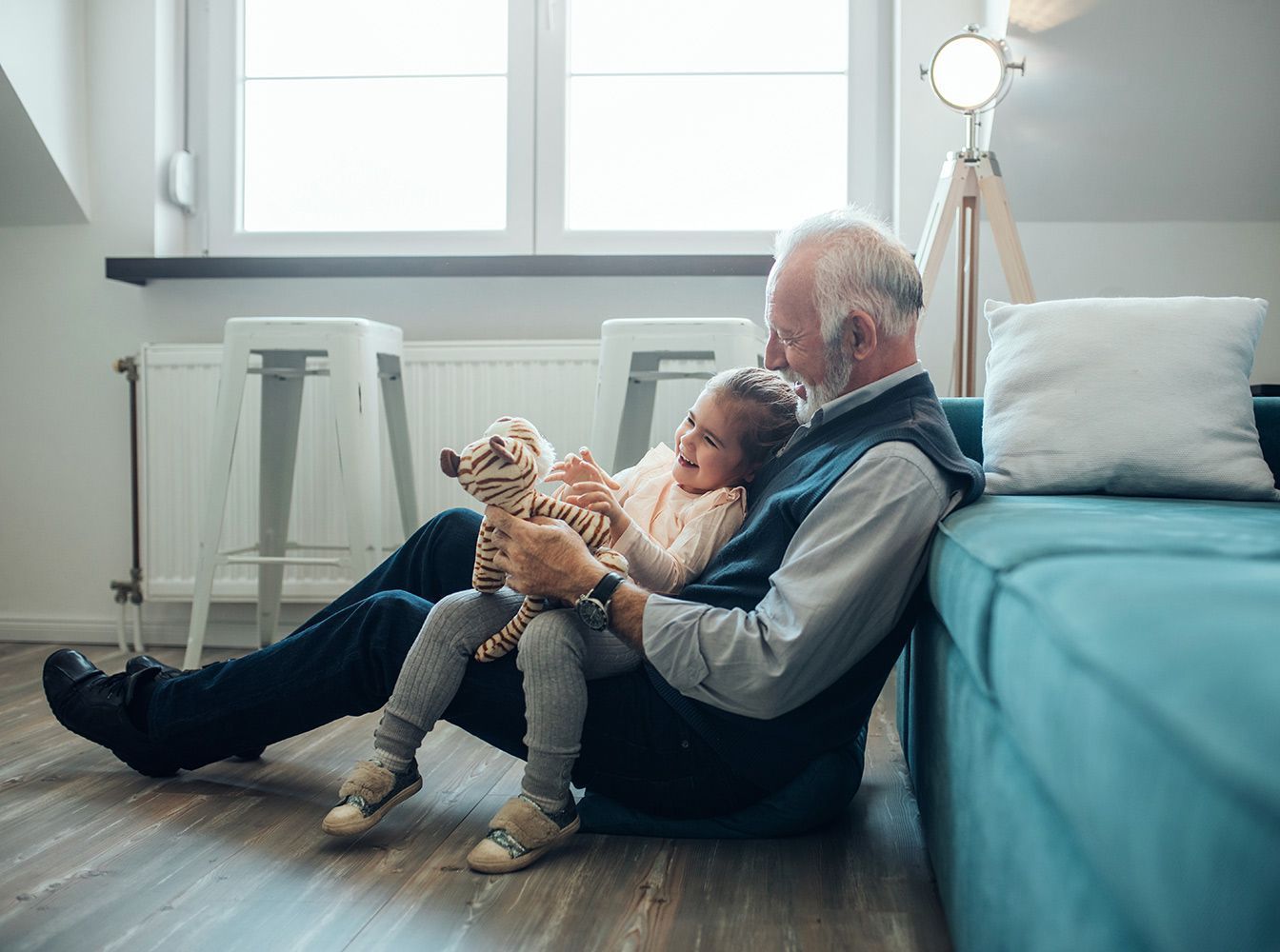 An elderly man is sitting on the floor with a little girl and a dog.
