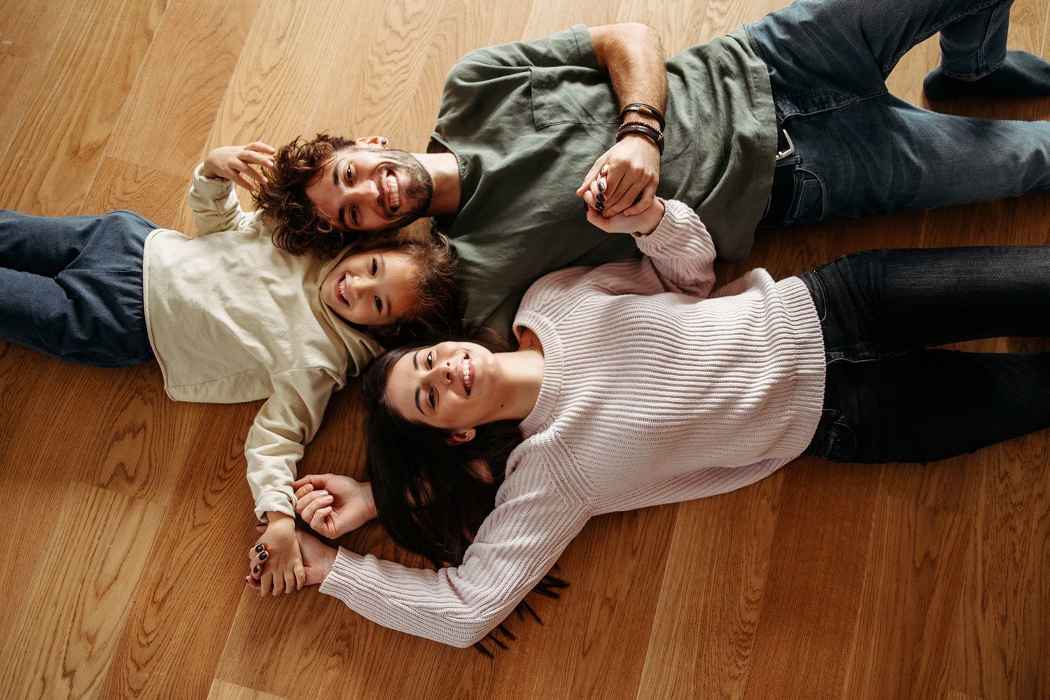 A family is laying on the floor holding hands.
