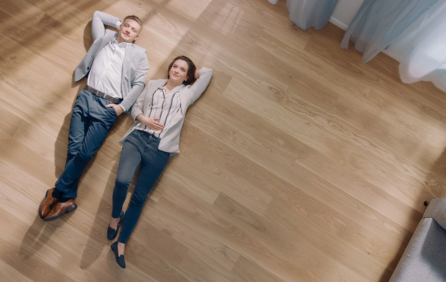 A man and a woman are laying on a wooden floor.