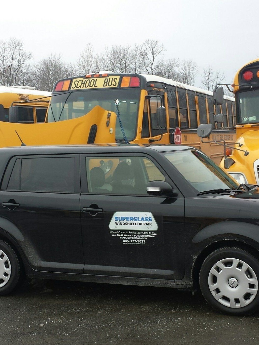 Black compact car parked in front of yellow school buses in a lot