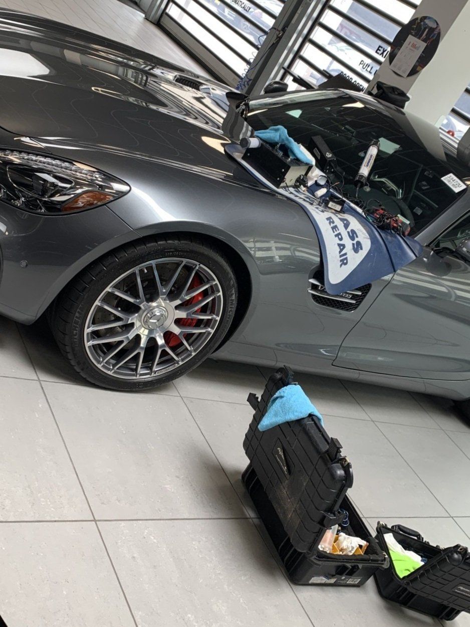 Gray sports car in showroom with open hood and luggage on the floor nearby
