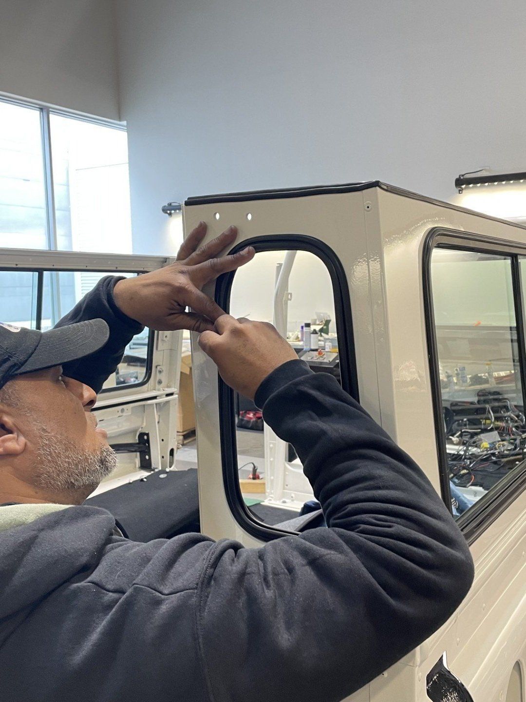 Worker installing a black-framed window on a white vehicle in a workshop
