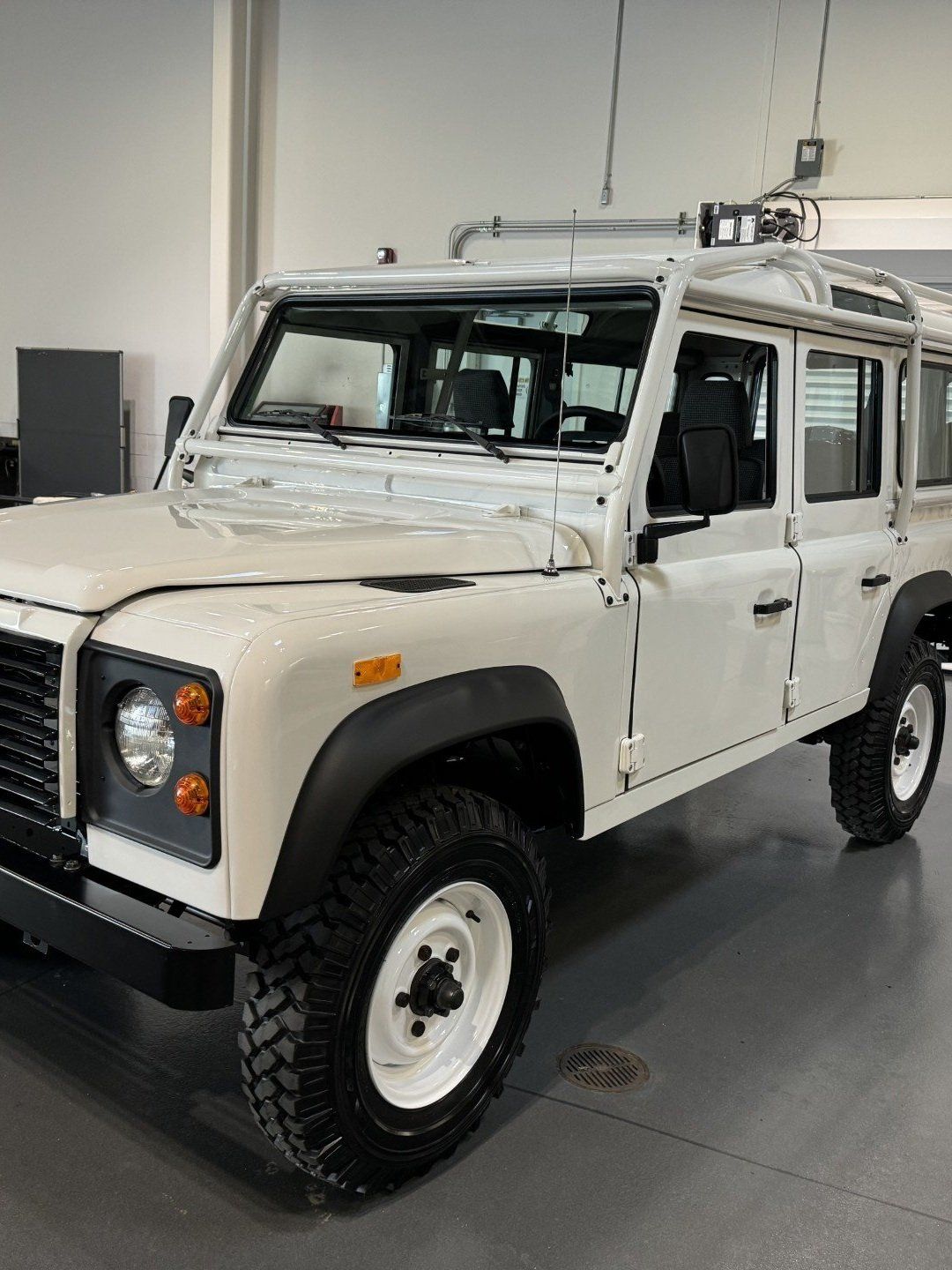 White off-road SUV with roof rack displayed indoors on a showroom floor