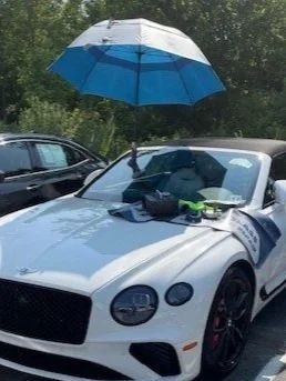 White sports car parked outdoors with a blue-and-white umbrella attached above the hood