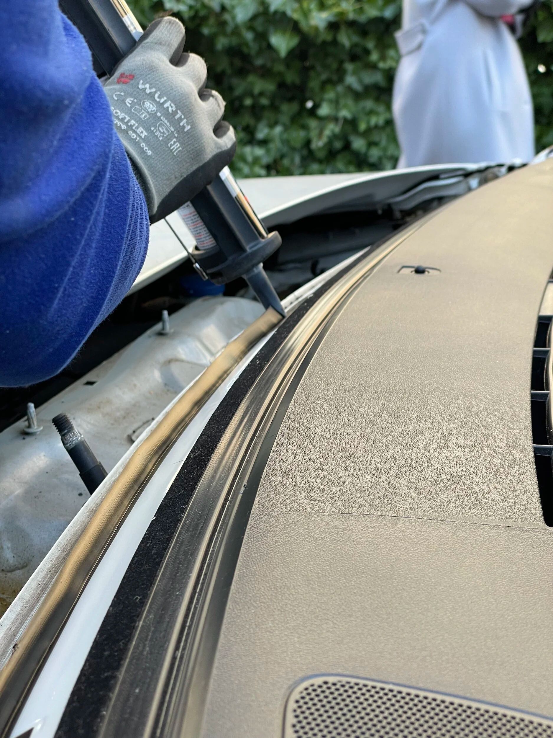 Gloved hand applying adhesive to a car windshield edge during repair